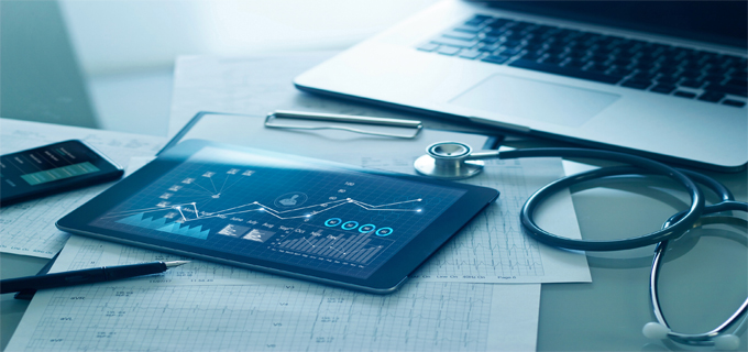 A tablet showing data sits next to a stethoscope and a laptop.
